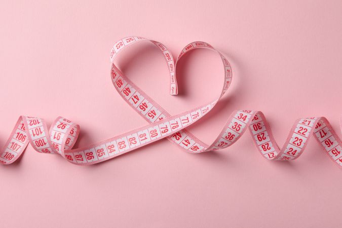 Measuring tape in the form of heart on pink background