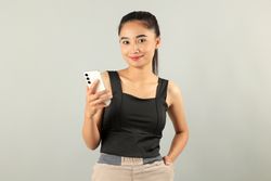 Young Asian Woman in Tank Top Facing Camera Holding Smartphone.