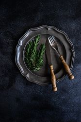 Table setting with dark plate with rosemary sprig