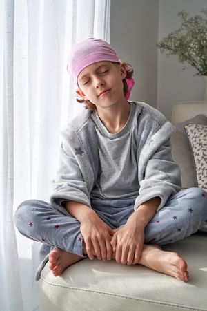 Relaxed boy in symbolic pink scarf sitting with crossed legs