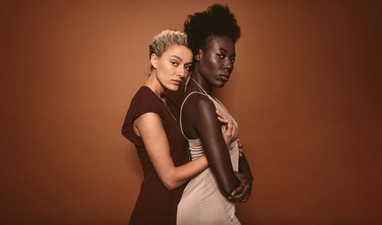 Portrait of two woman standing together over brown background