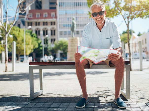 Happy man sitting on bench with a city map