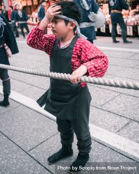 Boy wearing traditional celebration outfit grabbing a rope standing on street in Japan 5oKWg5
