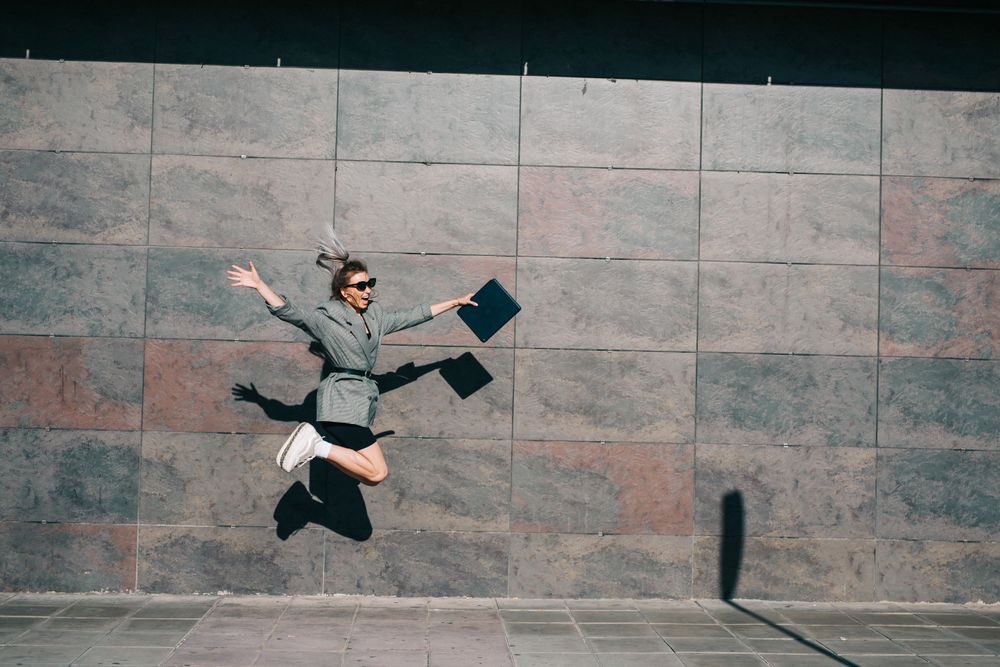 Woman joyfully jumping along wall with tablet