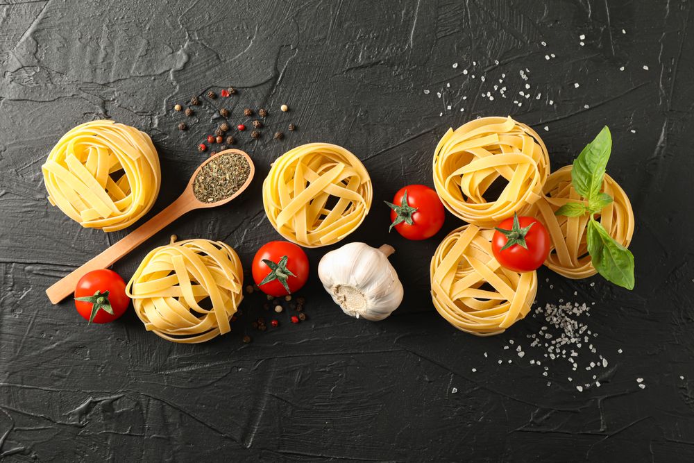 Flat lay composition with pasta, tomatoes, salt, garlic and spices on dark background, space for text