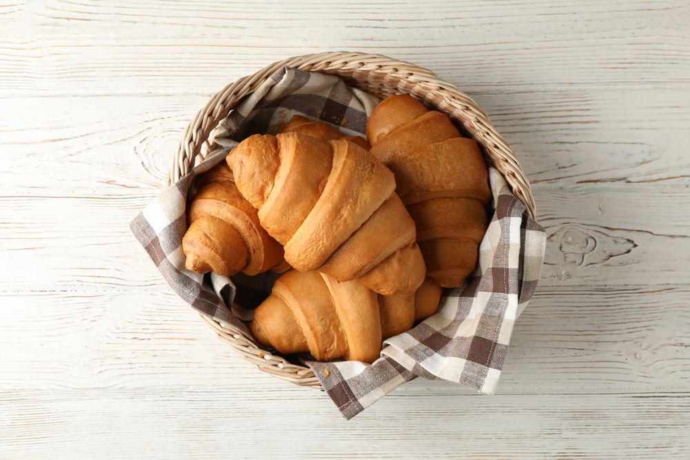 Top view of wicker basket with croissants on wooden table