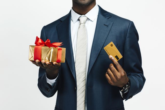 Image of cropped Black man holding present wrapped in gold paper and credit card