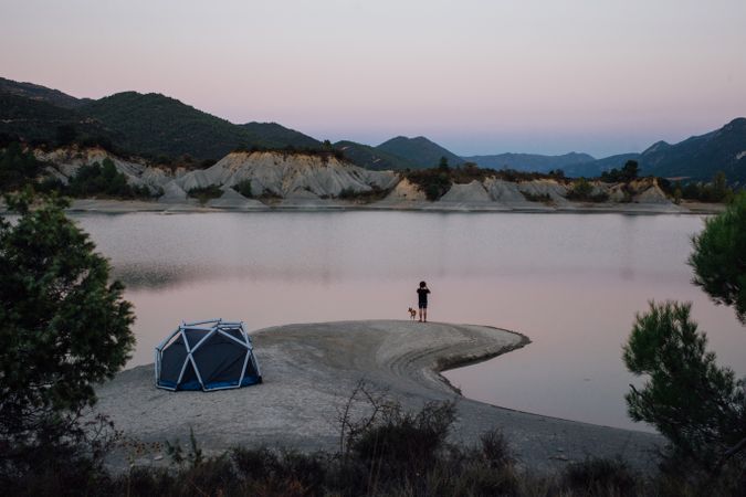 Man and dog looking over lake with tent at dusk