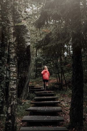 Woman in red jacket running on stairs between trees