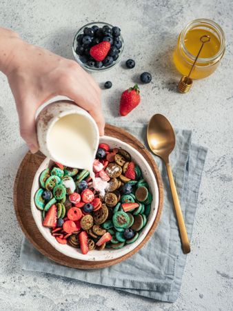 Person pouring sauce inside bowl of cereal and fruits