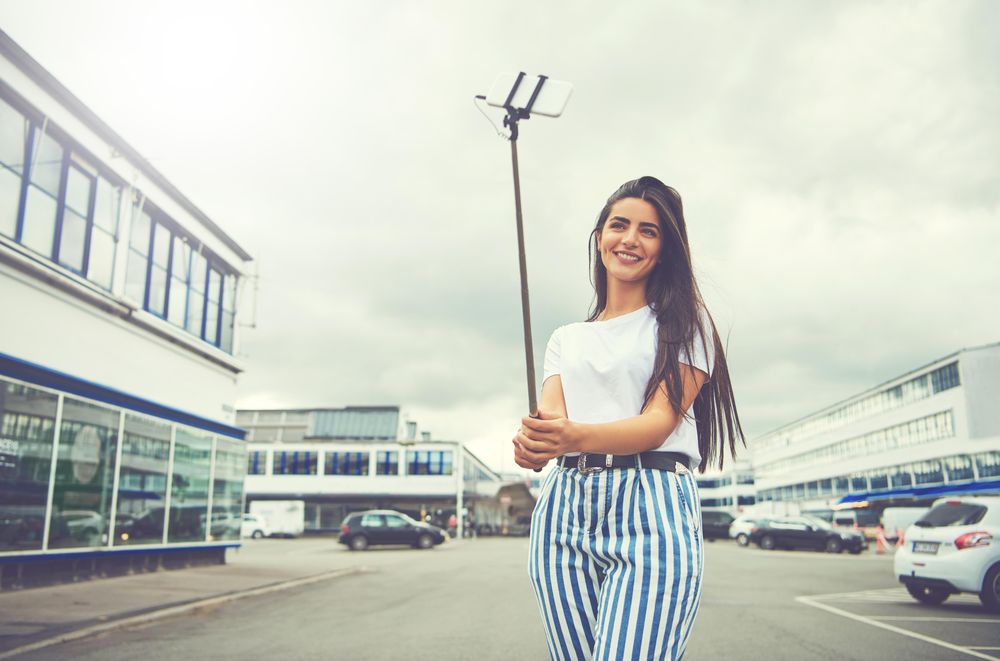 Woman smiling taking a selfie outside the back of buildings with cars parked