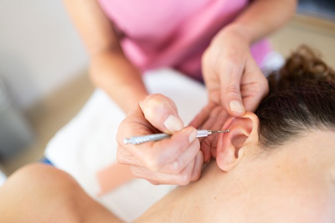Therapist using ear pen for auriculotherapy treatment female client