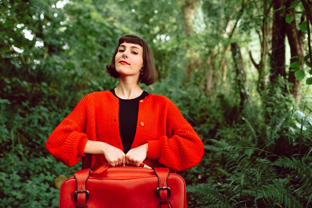 Woman in red with big red suitcase in forest