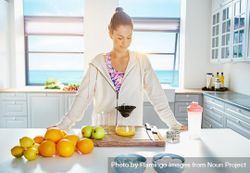 Fit woman in zip up hoodie making fresh fruit juice in kitchen bDweE4