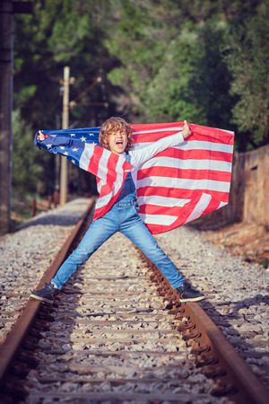 Joyful boy standing with USA flag on rails of railway