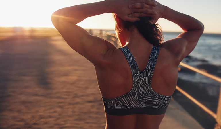 Rear view shot of muscular woman in sports bra at sunset