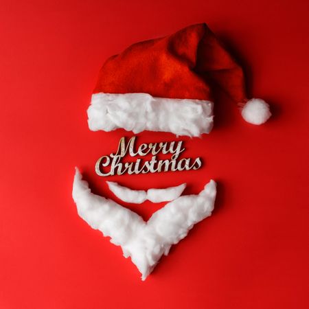 Santa hat and beard with mustache on red background with “Merry Christmas”
