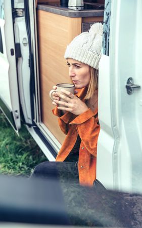 Female relaxing with coffee sitting on camper van step, close up vertical
