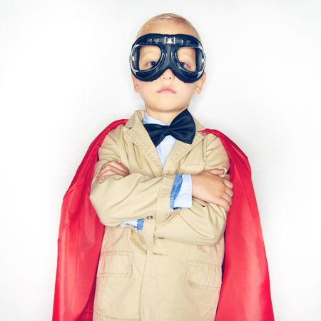 Serious blond boy wearing airplane goggles and cape