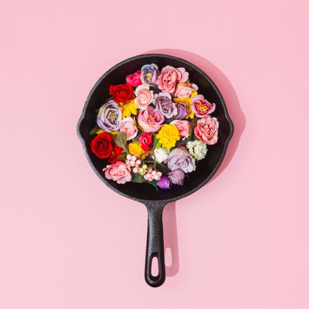 Flowers and green leaves in cast iron pan on pastel pink background