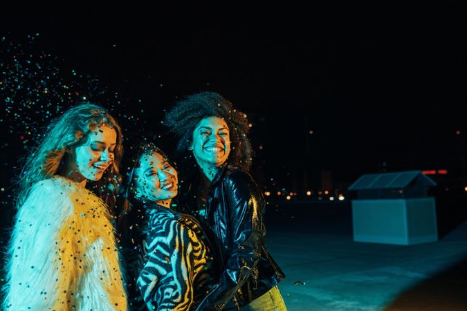 Group of female friends lit in green blue light at night surrounded in confetti