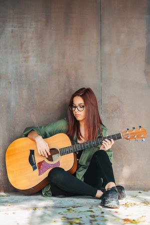 Romantic woman playing guitar leaning on wall