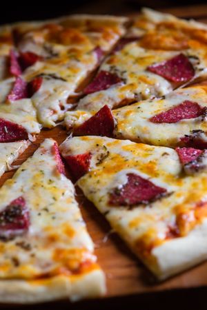 Close up of pizza with slices of meat on wooden board