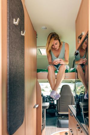 Female smiling in motorhome bunk bed while checking her phone