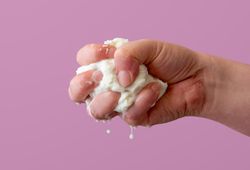 Squeezing mozzarella cheese in one hand, isolated on a purple background