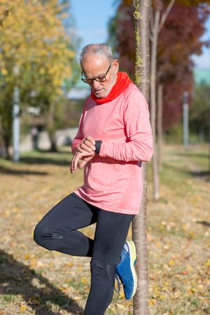 Older man leaning on tree checking watch in park