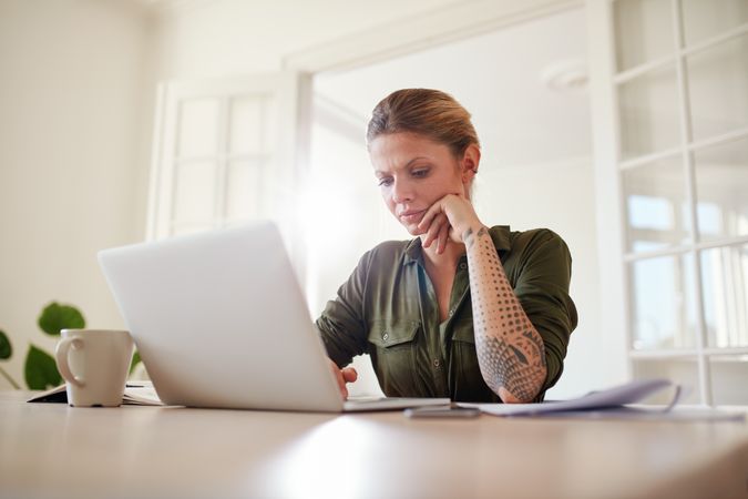 Indoor shot of beautiful female sitting at table and using laptop computer