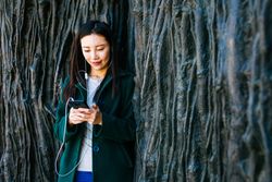 Asian female listening to music near rough wall