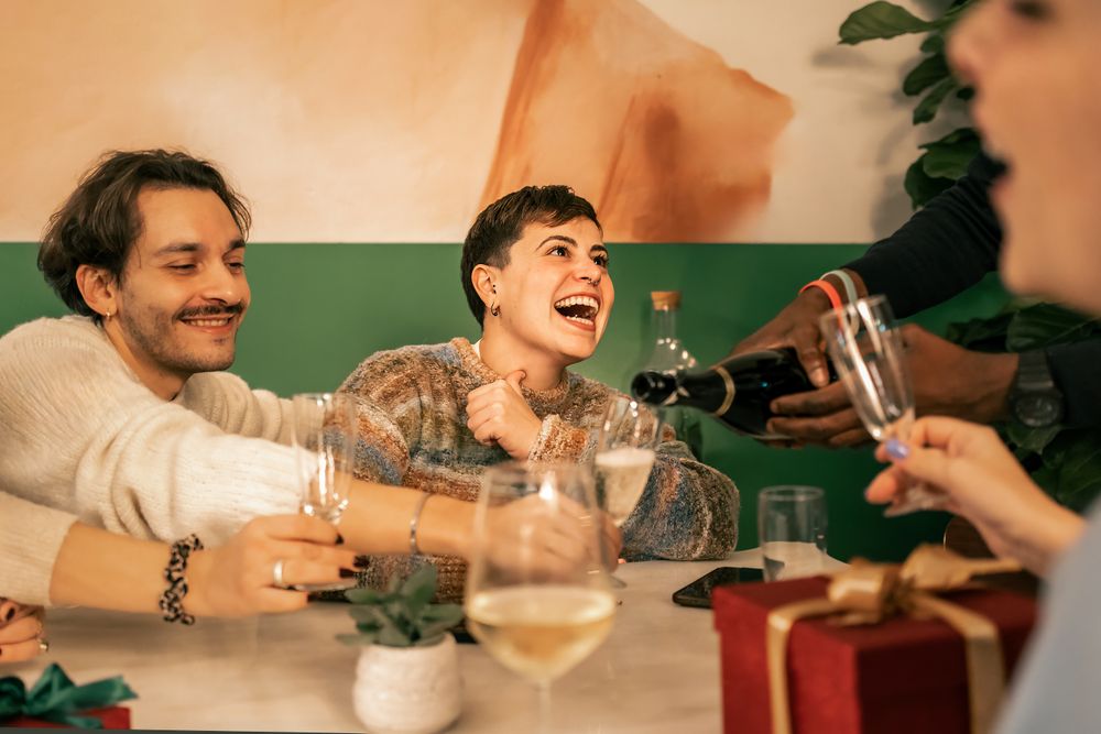 Joyful woman laughing while friends pour champagne at a Christmas celebration.