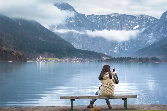 Woman on lakeshore taking pictures with her phone of Alpine scenery