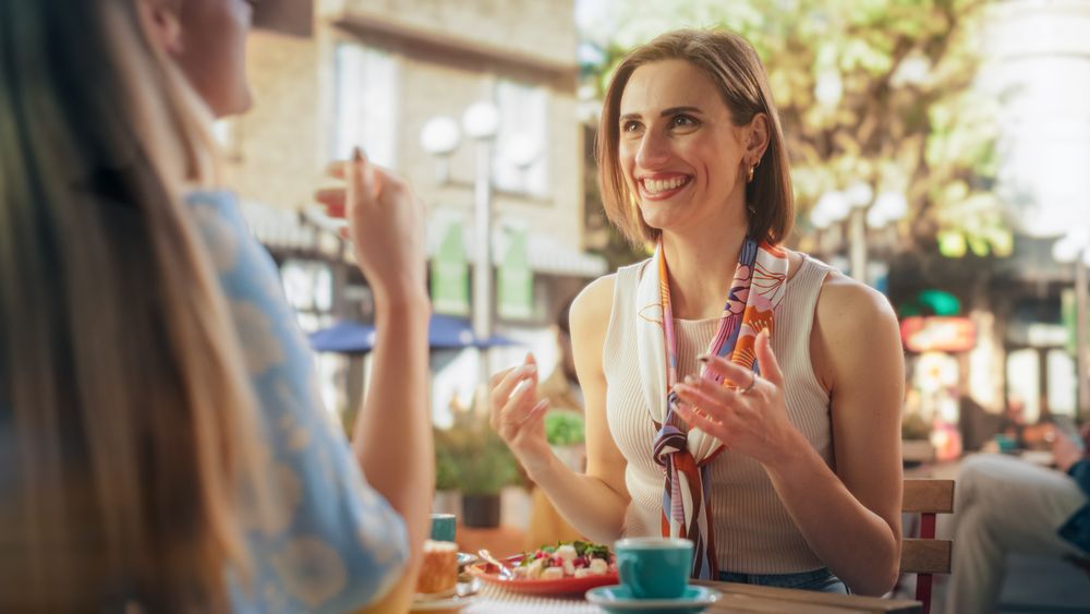 Two Female Friends Sitting in Front of Each Other in an Outdoors Restaurant, Eating Healthy Vegetarian Salad and a Dessert.