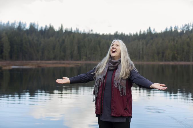 Happy woman with arms open looking up near lake