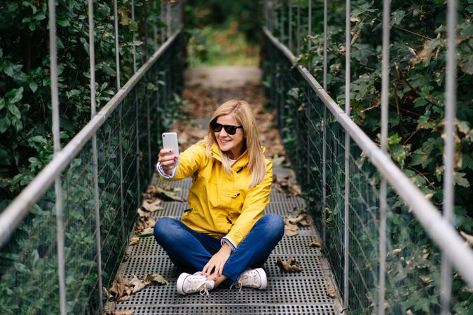 Happy female traveler taking selfie on suspension bridge in summer