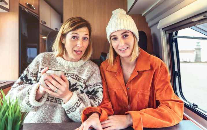 Female friends looking at camera as if talking on video call from back of camper van