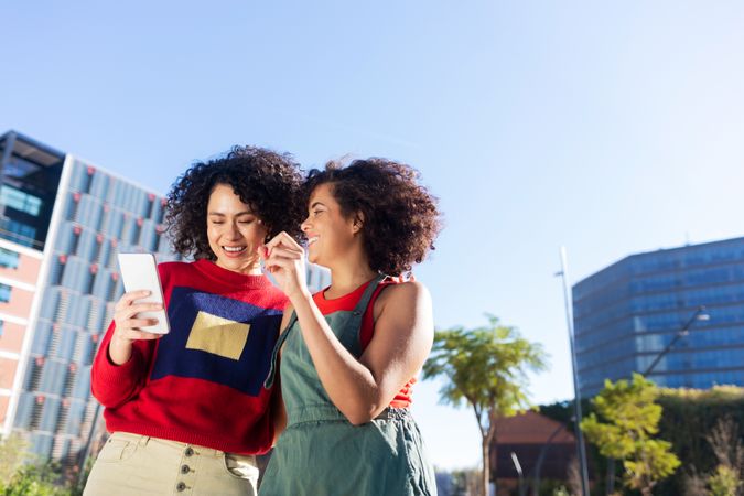 Female couple laughing over smartphone outside buildings