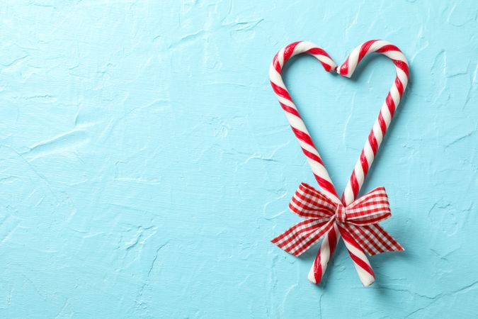 Sweet candy canes with bows on blue background, space for text