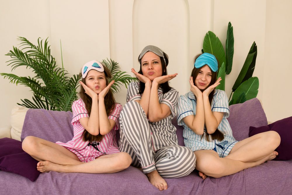Mother and daughters making playful faces while sitting on couch.