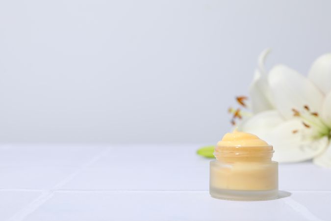 Jar with cream and lilies on light gray background, space for text