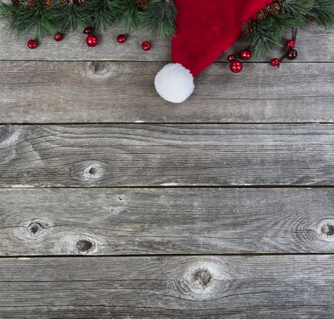 Merry Christmas or happy New Year background with fir tip branches and red Santa Claus cap on rustic wood