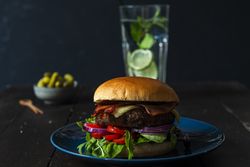 Burger on a blue plate water and pickels in the back