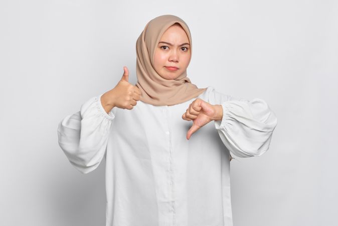 Asian female in headscarf with with hands making alternate thumb gesture