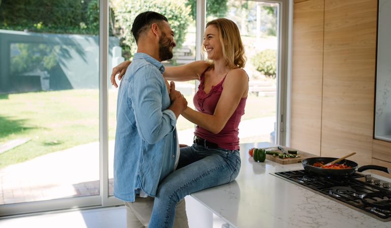 Woman sitting on kitchen counter with man standing