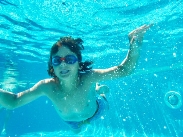 Funny boy swimming underwater looking at camera