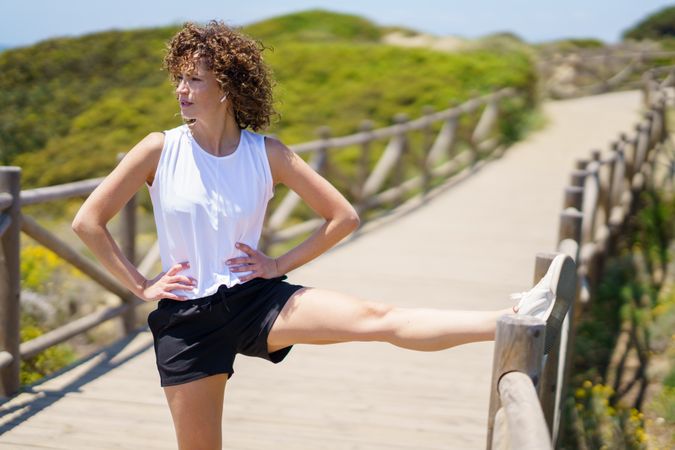 Slim young woman stretching leg on bridge in sunny day