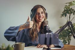 Smiling woman with headphones recording podcast and showing thumbs up gesture