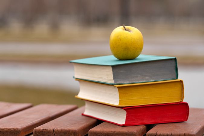 Yellow apple resting on top of colorful hardcover books.